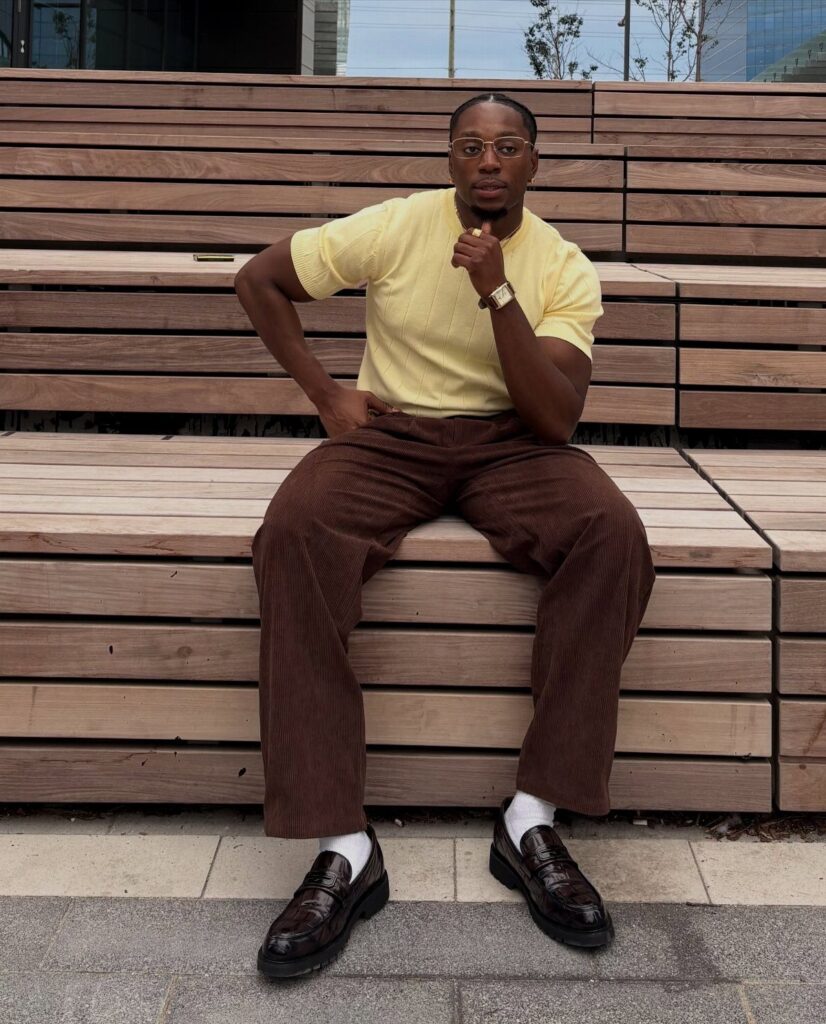 Man in yellow short-sleeved shirt and brown corduroy pants sitting on wooden steps.