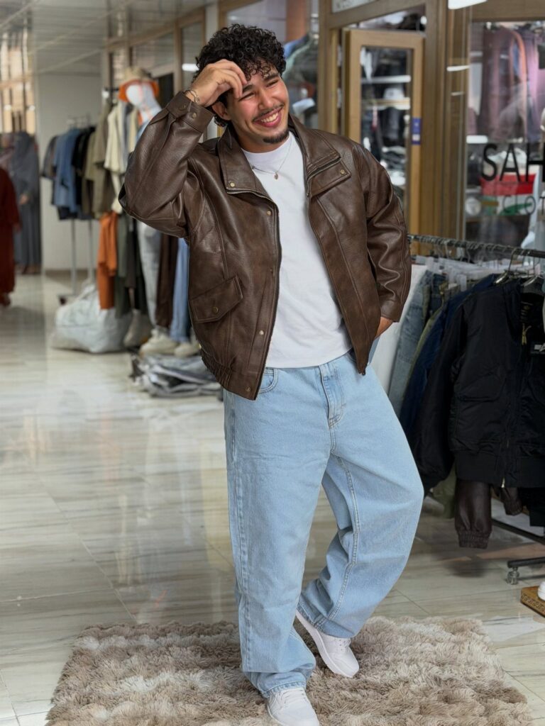 Man wearing a brown leather jacket and light blue wide-leg jeans in a store