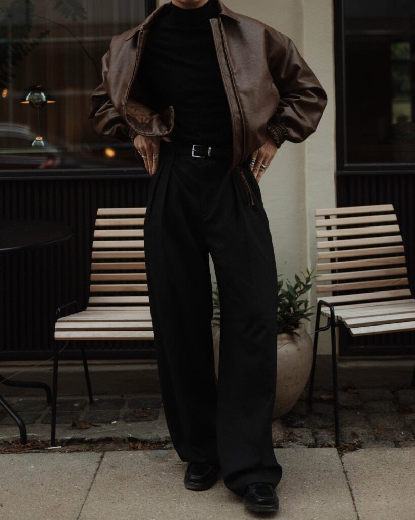 Person wearing a brown leather jacket with black turtleneck and wide-leg black trousers.