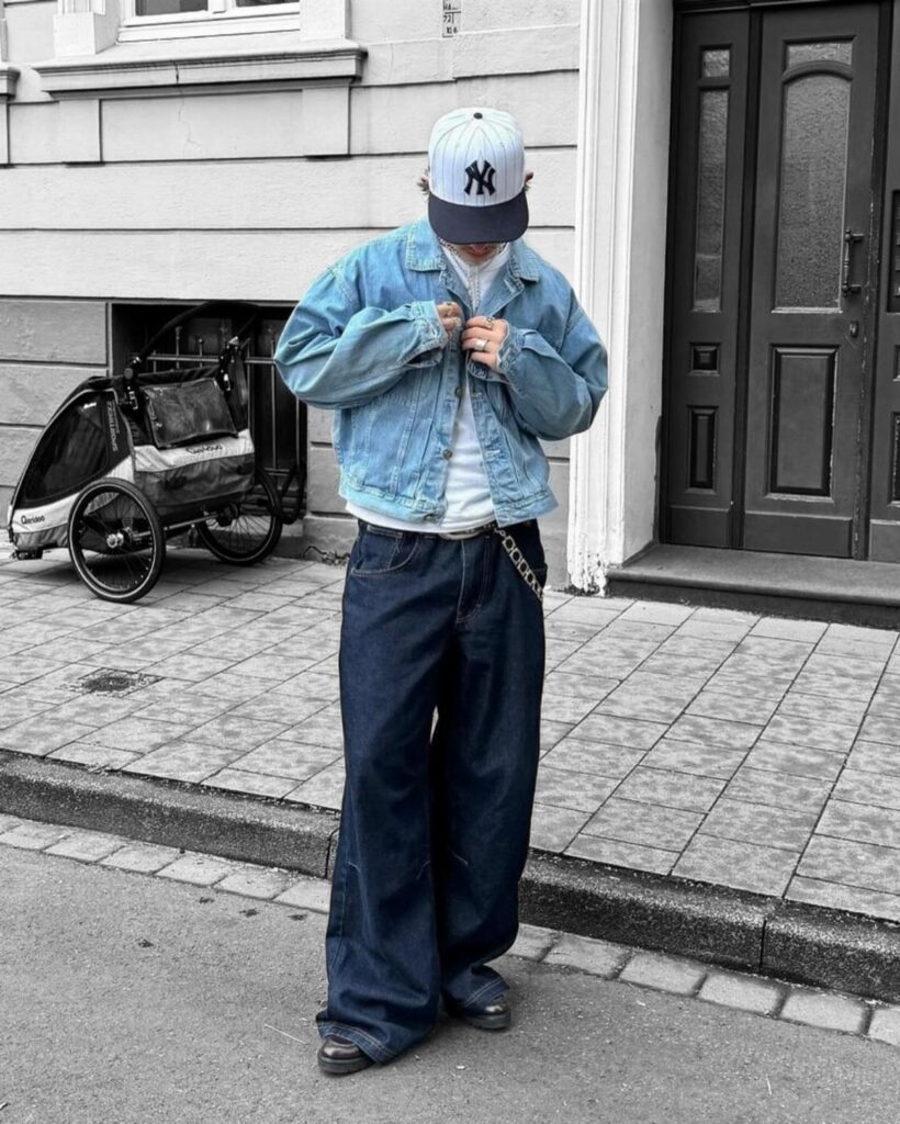 Person wearing a cropped denim jacket and wide-leg jeans standing on a city sidewalk.