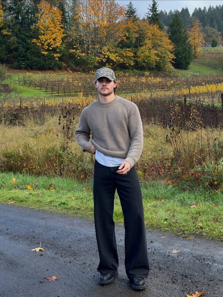 Man wearing a brown knit sweater and black wide-leg trousers in autumn landscape