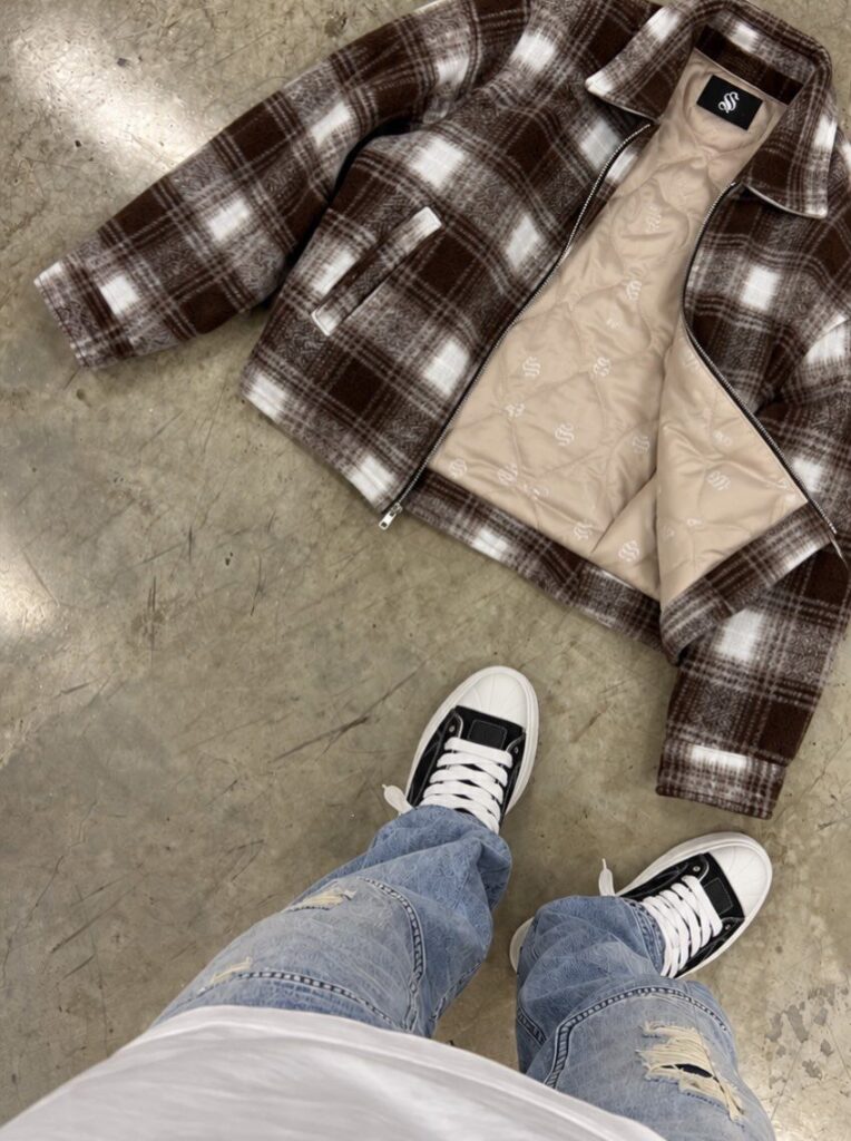 Brown and white plaid jacket on concrete floor next to ripped blue jeans.