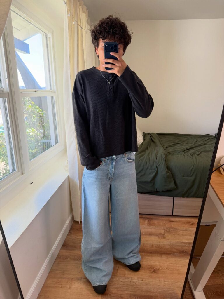 Person wearing a black long-sleeved shirt and wide-leg light blue jeans in a bedroom.