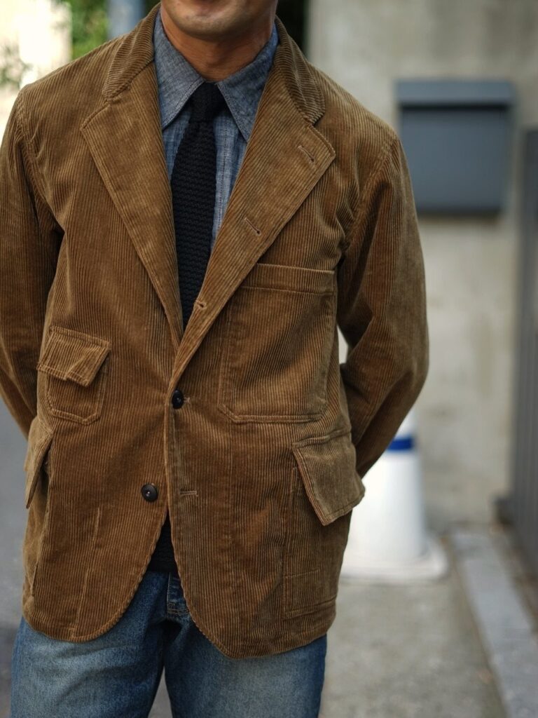 Brown corduroy blazer worn with a blue shirt, dark tie, and blue jeans.