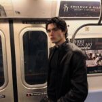 Young man wearing a black leather jacket posing inside a subway train car.