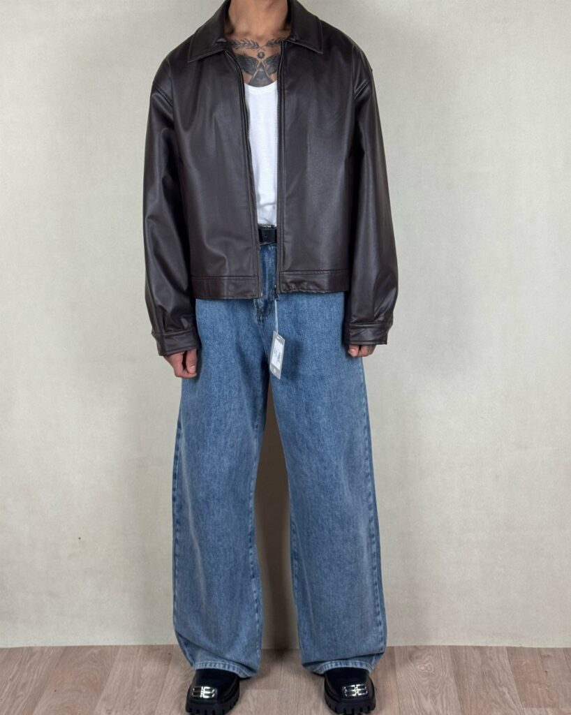 Person wearing a brown leather jacket, white t-shirt, and wide-leg blue jeans.