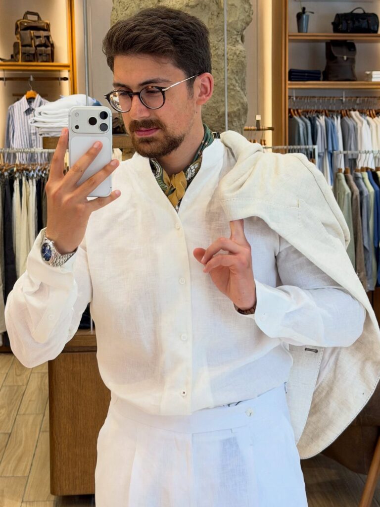 Man in white linen shirt and trousers posing for a mirror selfie in store