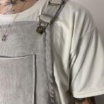 Light grey corduroy bib overalls worn over a white t-shirt with metal buckles.