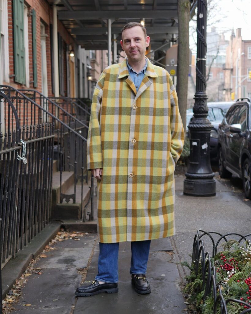 Man wearing a yellow and grey large-check plaid trench coat on a city street