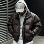 Man wearing a brown puffer jacket, grey hoodie, and white baseball cap.