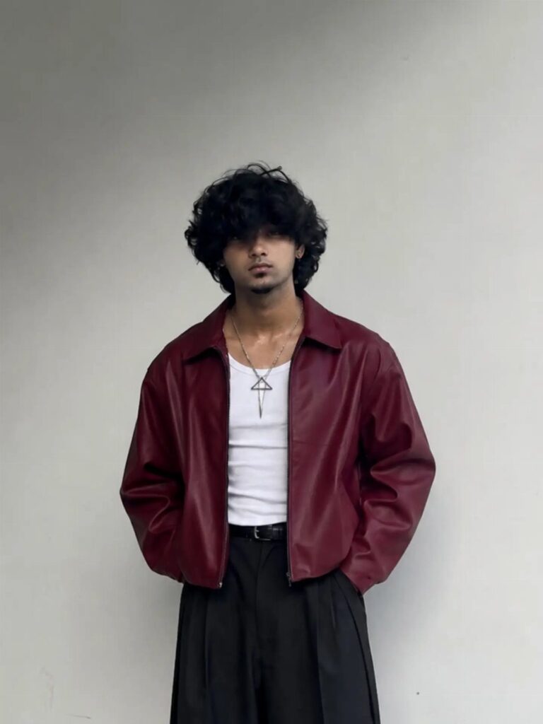 Person wearing a dark red leather jacket, white tank top, and black trousers.