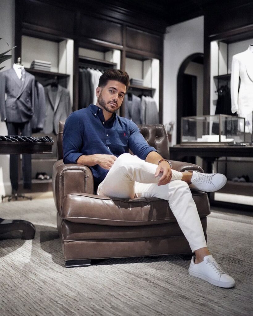 Man in navy shirt and white pants sitting in a luxury clothing store.