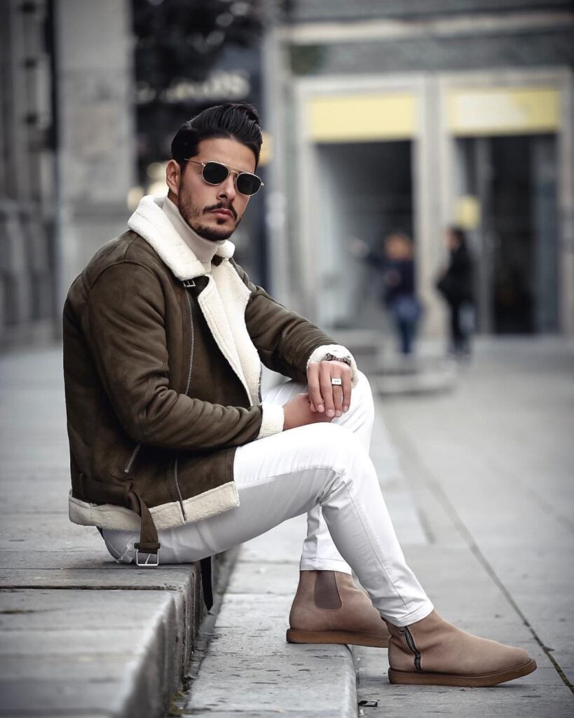 Man in brown shearling jacket and white pants wearing tan suede Chelsea boots.