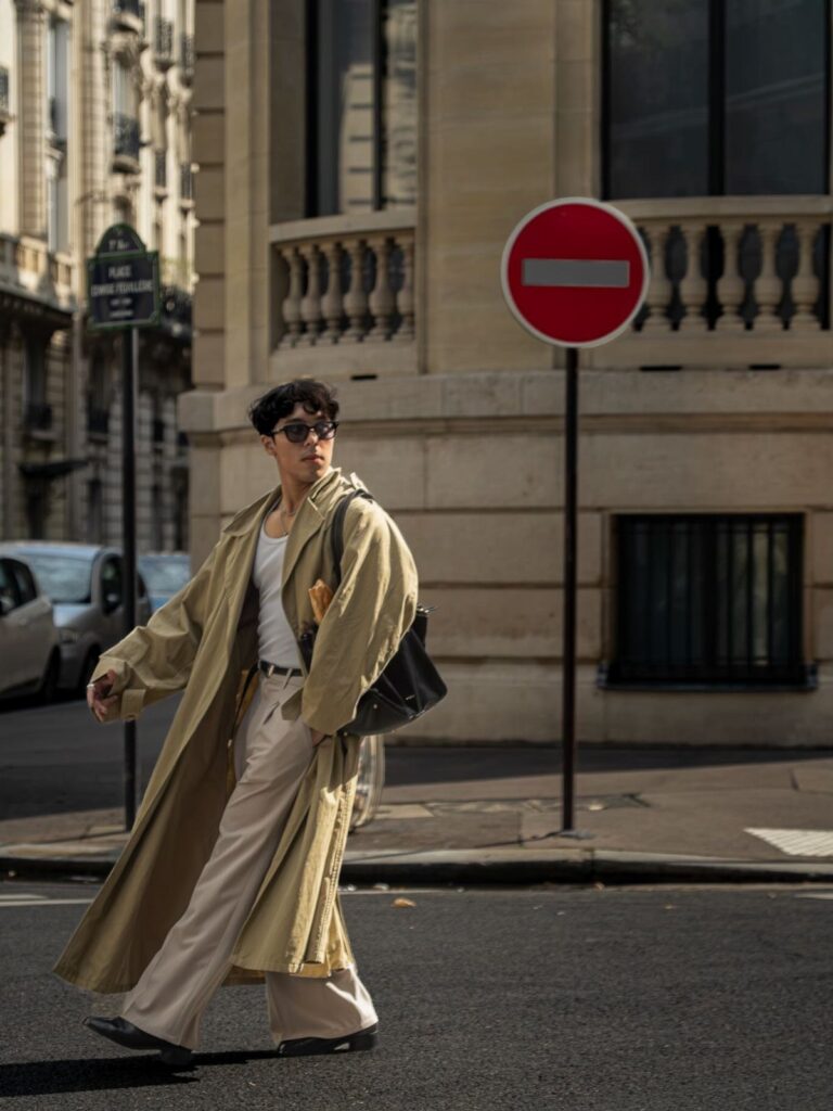 Person walking in a city wearing a beige trench coat and cream trousers.
