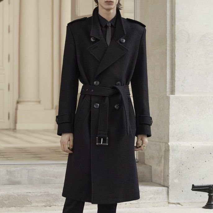 Man wearing a tailored black double-breasted wool trench coat with a belted waist.
